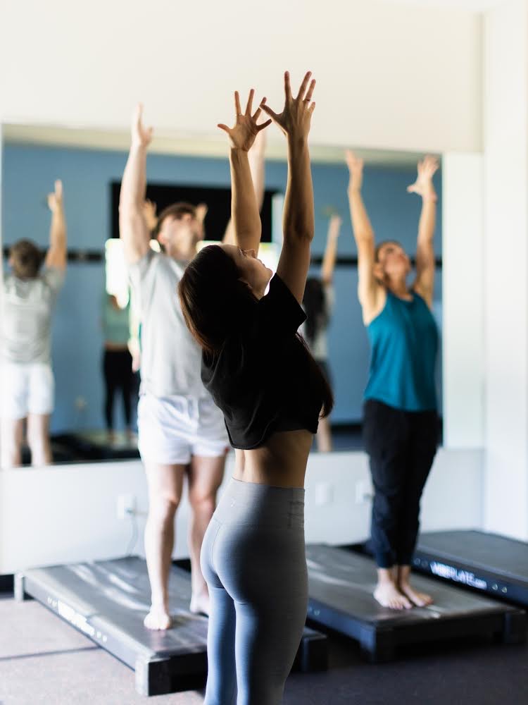 Kymber leading a class through a sun salutation, students reaching arms overhead